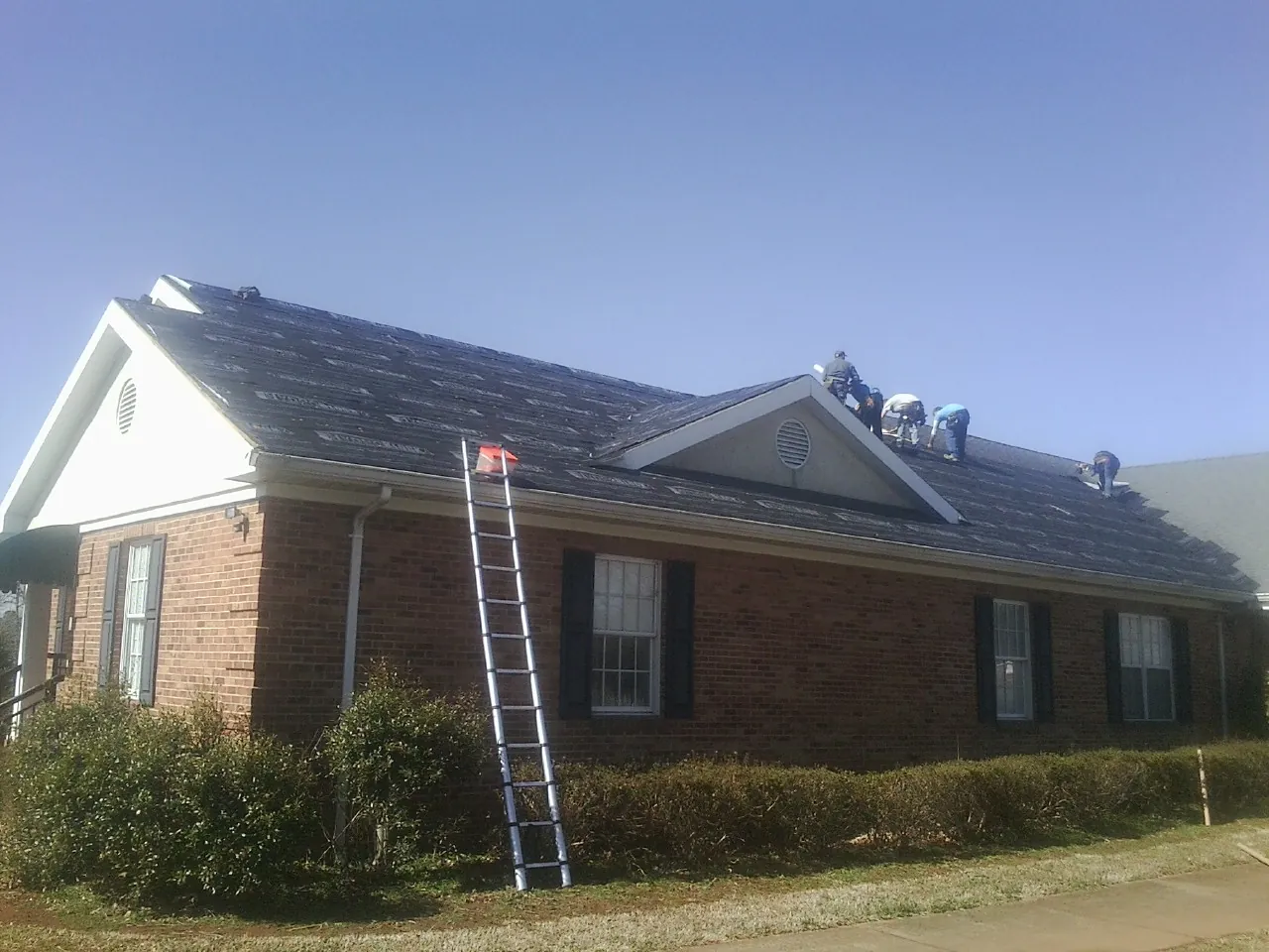 Crew tearing shingles off a brick ranch roof with a ladder set — Emergency Roof Repair work by our crew in Kingston